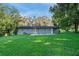 Exterior rear view of a home with a grassy yard and patio, shaded by mature trees providing a serene backdrop at 211 Sara Ln, Leesburg, FL 34748