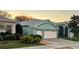 A partial street view of a home showcasing a spacious two-car garage, turquoise exterior and well kept lawn at 25517 Laurel Valley Rd, Leesburg, FL 34748