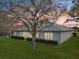 Exterior back of home showing a large green lawn, shrubbery and a tree during a sunset at 26821 Augusta Springs Cir, Leesburg, FL 34748