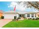 Charming single story home with a well-manicured lawn, an American flag, and an attached two-car garage at 26821 Augusta Springs Cir, Leesburg, FL 34748