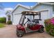 Charming light blue home exterior with a red golf cart, white garage doors, and beautiful landscaping at 509 Ventura Ct, The Villages, FL 32159