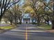 Long driveway lined with mature trees leading to stately white building; lush lawns and landscaping at 25527 Oak Aly, Leesburg, FL 34748