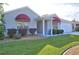 Charming single-story home featuring manicured lawn, well-maintained landscaping, and red awnings over the windows at 1229 Augustine Dr, The Villages, FL 32159