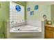 Bright bathroom featuring a tiled corner soaking tub with a glass block window, and light green walls at 24104 Robinwood St, Leesburg, FL 34748