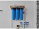 Close-up of three blue Nova water filters and gauges mounted on the wall of a garage, ensuring clean water at 5978 Conley Ct, The Villages, FL 32163