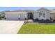 Inviting home exterior featuring a two-car garage, landscaped front yard, and a welcoming brick walkway to the front door at 6083 Delphina Loop, The Villages, FL 32163