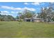 Rear view of home and large backyard, featuring lush green grass and mature trees under a sunny sky at 7729 Lake Andrea Cir, Mount Dora, FL 32757