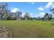 Expansive backyard featuring lush green grass, scattered trees, and a glimpse of the home's screened-in porch at 7729 Lake Andrea Cir, Mount Dora, FL 32757