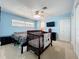 Light blue bedroom featuring a bed, crib, ceiling fan, and a wall-mounted TV at 1108 Cedar St, Leesburg, FL 34748