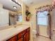 Well-lit bathroom featuring a cherry wood vanity, neutral countertops, floral curtains, and a large framed mirror at 27023 Old English Ct, Leesburg, FL 34748