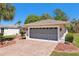 Attached two-car garage with brick paved driveway complemented by beautiful landscaping and blue skies at 32800 Oak Park Dr, Leesburg, FL 34748