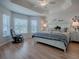 Cozy bedroom featuring tray ceiling, plush bedding, and comfortable reading chair by the window at 2922 Rain Lily Loop, The Villages, FL 32163