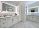 Bright bathroom featuring double vanities, custom cabinets, gorgeous countertops, and elegant, illuminated mirrors at 464 Long & Winding Rd, Groveland, FL 34736
