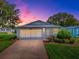 Charming home featuring a manicured lawn, attached garage, and inviting entrance amid a lovely sunset backdrop at 701 Cottage Park Ln, Leesburg, FL 34748