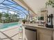 Screened-in pool area featuring a granite bar, mini fridge, and views of the backyard and adjacent foliage at 12136 Se 176Th Loop, Summerfield, FL 34491