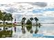 Picturesque lake view featuring a charming lighthouse and palm trees against a partly cloudy sky, with reflections on the water at 219 N Rossiter St, Mount Dora, FL 32757