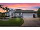 Charming single-story home with a two-car garage, lush landscaping, and a beautifully manicured front yard at sunset at 22247 Draw Bridge Dr, Leesburg, FL 34748