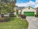 Charming single-story home with lush landscaping, a green two-car garage door, and a brick driveway at 24112 Robinwood St, Leesburg, FL 34748