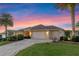 Attractive home with a spacious three-car garage, lush landscaping, and a brick driveway under a colorful sky at 2428 Maverick Way, The Villages, FL 32162