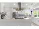 Open-concept kitchen boasts white cabinetry, stainless steel appliances, a modern range hood, and large windows at 6106 Spinnaker Loop, Lady Lake, FL 32159