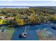 An aerial shot displays a covered dock extending into a tranquil lake surrounded by verdant trees and a clear blue sky at 15749 Acorn Cir, Tavares, FL 32778