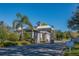 Community gatehouse with gray siding, stone accents, lush landscaping, and clear blue skies at 5441 Sea Leopard St, Tavares, FL 32778