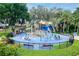 Community water park with playground and splash pad on a blue surface, enclosed by a black fence and manicured lawn at 5441 Sea Leopard St, Tavares, FL 32778