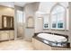 Luxurious bathroom features a soaking tub with marble surround and an arched window with plantation shutters at 10417 Lake Louisa Rd, Clermont, FL 34711