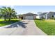 View of the driveway leading to the attached garage, surrounded by lush green grass and landscaping at 1310 Leone Ln, The Villages, FL 32159