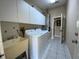 Well-lit laundry room with white cabinets and appliances, including a sink and door to the hallway at 664 San Pedro Dr, The Villages, FL 32159