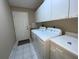 Well-lit laundry room with white cabinets, tile floor, and appliances, with a door leading to the garage at 664 San Pedro Dr, The Villages, FL 32159