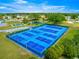 Aerial view of community tennis courts with vibrant blue surfaces, surrounded by lush greenery and a scenic pond at 9773 Se 179Th Pl, Summerfield, FL 34491