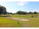 Scenic golf course view featuring lush green fairways, mature trees, and a sand bunker on a sunny day at 9948 Se 175Th Pl, Summerfield, FL 34491