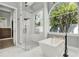 Bright bathroom features a glass-enclosed shower and modern soaking tub beneath a large arched window at 13112 Luntz Point Ln, Windermere, FL 34786