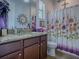 Charming bathroom featuring granite countertop, updated cabinets, decorative mirror, and a floral shower curtain at 1408 Deuce Cir, Davenport, FL 33896