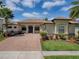 Inviting home featuring a brick paver driveway, lush landscaping, and a well-maintained lawn under a bright blue sky at 1408 Deuce Cir, Davenport, FL 33896