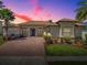 Charming home showcasing a paver driveway, manicured lawn, and lush landscaping with palms against a vibrant twilight sky at 1408 Deuce Cir, Davenport, FL 33896
