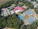 Aerial view of community clubhouse, pool, parking, and tennis courts surrounded by mature trees and lush landscaping at 26535 Deuce Ct, Leesburg, FL 34748