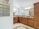 The main bathroom with double sinks, a large mirror, a glass block window, and wood cabinets at 2992 Hicks Pl, The Villages, FL 32163