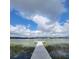 Scenic view of lake with a wooden dock and seating, surrounded by aquatic plants and a cloudy sky at 11024 Windchime Cir, Clermont, FL 34711