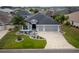 Overhead view of a gray home with a three-car garage, surrounded by green lawns, landscaping, and mature palm trees at 3942 Zenith Loop, The Villages, FL 32163