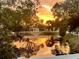 Scenic sunset view of a tranquil pond with a fountain, surrounded by lush trees and a white fence at 501 Santa Fe Rd, Tavares, FL 32778