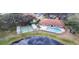 Aerial view of community pool, shuffleboard court, and clubhouse nestled within lush trees near a pond at 74 Stone Haven Ct, Leesburg, FL 34788