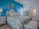 Bright main bedroom with a blue accent wall features a plush bed, a sitting bench, and light wood floors at 1010 Ventura Dr, The Villages, FL 32159