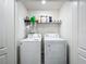 A well-lit laundry closet with a washing machine, dryer, and storage shelf with laundry supplies at 11995 Callicarpa Ln, Leesburg, FL 34788