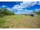 Expansive grassy pasture with a charming wooden shelter and perimeter fencing against a blue sky at 15141 Farm Rd, Groveland, FL 34736