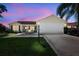 Charming single-story home with a well-manicured lawn, inviting patio, and two-car garage, set against a colorful sunset sky at 2290 Due West Dr, The Villages, FL 32162
