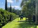 A black horse grazes in a green pasture behind a metal gate, surrounded by lush trees and manicured hedges at 3511 Fox Lake Dr, Apopka, FL 32712