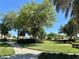 Manicured community green space featuring a walking path, lush landscaping, and mature trees under a bright blue sky at 728 Ramirez Ave, The Villages, FL 32159