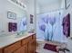 Well-lit bathroom featuring a shower with purple floral curtain and wood cabinets at 11702 Se 173Rd Lane Rd, Summerfield, FL 34491